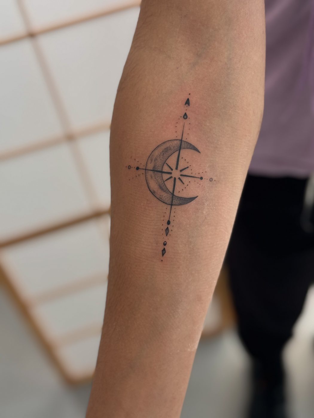 Tatuaje de línea fina con brújula y luna en el antebrazo